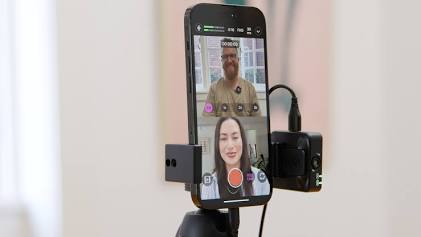 A smartphone mounted on a tripod recording a two-person video podcast interview, showing the lean mobile setup used for guerrilla podcasting.